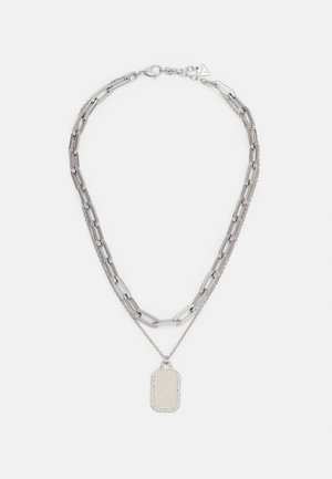 Collier double chaîne en argent avec de grandes mailles et une chaîne plus petite tenant un pendentif rectangulaire bordé de petits cristaux.