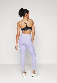 Un sutien sport negru cu logo alb Nike, combinat cu colanți violeți deschiși cu talie înaltă, prezentând o bandă albă "PKE", purtați cu adidași albi.