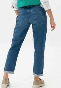 Lehké modré džíny s rovnými nohavicemi, ohrnutými manžetami a dvěma zadními kapsami. Nosené s béžovými platformovými botami.