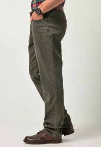 Jeans verde oliva in denim, con un design a gamba dritta, tasche frontali e leggeri segni di usura. Scarpe in pelle marrone visibili.