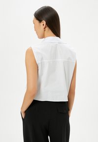 Witte mouwloze blouse met een cropped ontwerp, voorzien van een gladde textuur en strakke lijnen, gedragen met zwarte op maat gemaakte broeken.