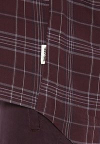 Maroon plaid shirt with white and purple lines, featuring a straight hem and a small label on the side. Soft fabric texture.