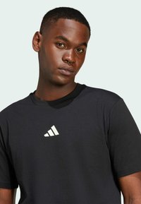 Svart t-shirt i mjukt tyg, med rund halsringning och korta ärmar, med en vit Adidas-logotyp på framsidan.