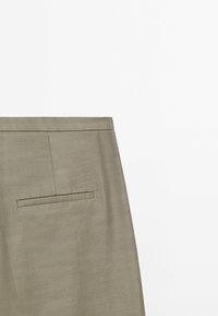 Gros plan sur un pantalon de couleur kaki montrant la ceinture et une poche passepoilée simple sur le côté droit arrière.