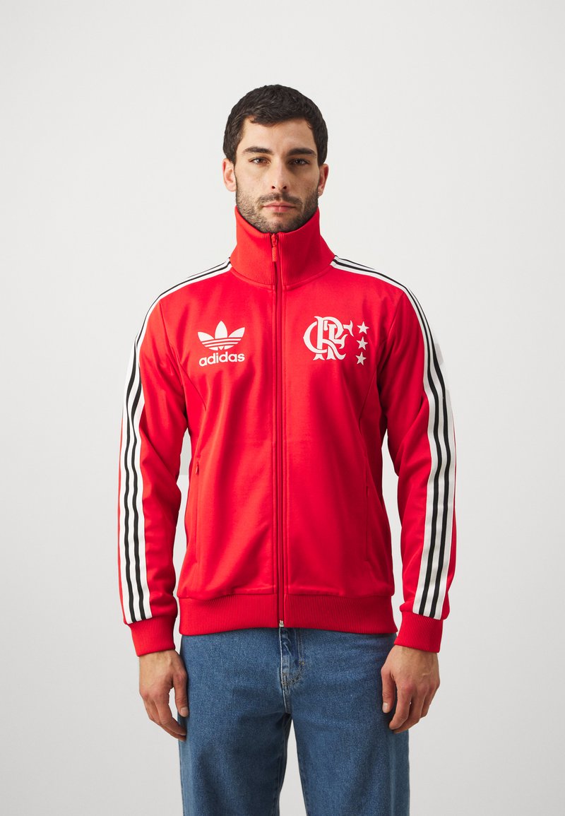 Red zip-up jacket with high collar, black and white striped sleeves, Adidas logo, and a team emblem featuring stars on the chest.