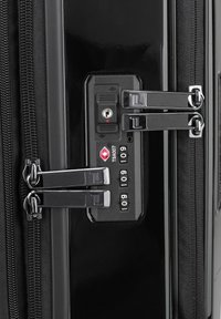 Maleta rígida negra con cremalleras de metal dobles y candado de combinación TSA. Superficie lisa con un acabado brillante y ligeros acentos de textura.