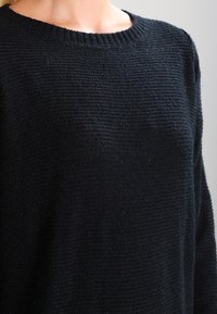 Svart stickad tröja med ribbad rund halsringning som visar upp ett texturerat tyg. Designen är enkel, med en mysig, avslappnad passform.