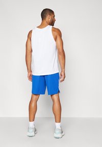 Fehér hálós trikó, kék rövidnadrág fehér oldalsávokkal, és szürke sportcipő. A modell hátulról látható.