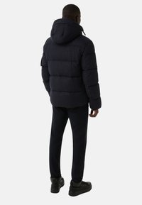 Ciemnogranatowa puchowa kurtka z kapturem, z pikowanym wzorem i elastycznymi mankietami. W zestawie z ciemnymi spodniami i czarnymi masywnymi trampkami.