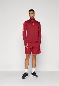 Weinrotes Sportset mit langärmligem Reißverschluss-Oberteil mit roten Akzenten und passenden Shorts. Komplett mit schwarzen Turnschuhen und weißen Socken.