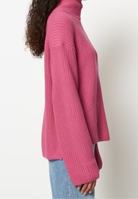 Pull à col roulé tricoté rose avec une coupe décontractée, une texture côtelée et des coutures d'épaule tombantes, associé à un jean en denim clair.