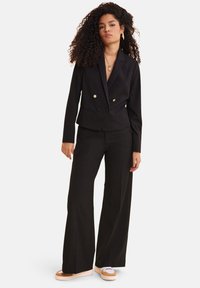 Blazer doppiopetto nero con bottoni dorati abbinato a pantaloni a gamba larga. Tessuto liscio, linee pulite e design minimalista.