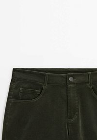 Pantalon en velours côtelé vert foncé avec poches avant, passants de ceinture et fermeture par bouton à la taille sur fond blanc.