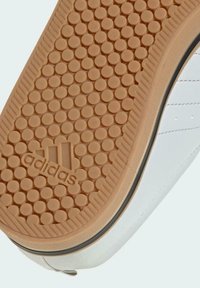 Suela de zapato con patrón de dibujo circular, suela exterior de goma color marrón claro, parte superior blanca con costuras y logotipo de Adidas grabado en el centro de la suela.