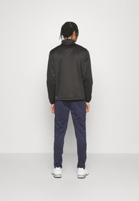 Černá zipová bunda s vysokým límcem, doplněná námořnickými zúženými kalhotami. Tkanina vypadá hladce, má minimalistický design a žádné viditelné logo.