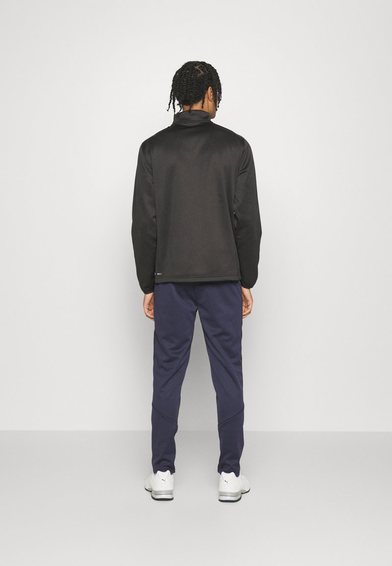 Černá zipová bunda s vysokým límcem, doplněná námořnickými zúženými kalhotami. Tkanina vypadá hladce, má minimalistický design a žádné viditelné logo.