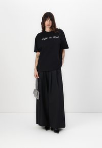 Črn oversized T-shirt z belim pisanim napisom, v kombinaciji s širokimi črnimi nabranimi hlačami. Majhna srebrna torbica dopolnjuje obleko.