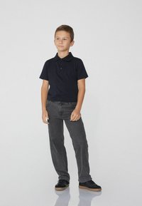 Námořnická polokošile s límečkem a třemi knoflíky, spárovaná s tmavě šedými džíny a černými teniskami s hnědou podrážkou. Jednoduché, neformální oblečení.