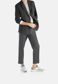 Grau gestreifter Doppelreiher-Blazer über einem hellgrauen Hemd, kombiniert mit maßgeschneiderten grauen Hosen und mehrfarbigen Sneakern mit blauen Akzenten.