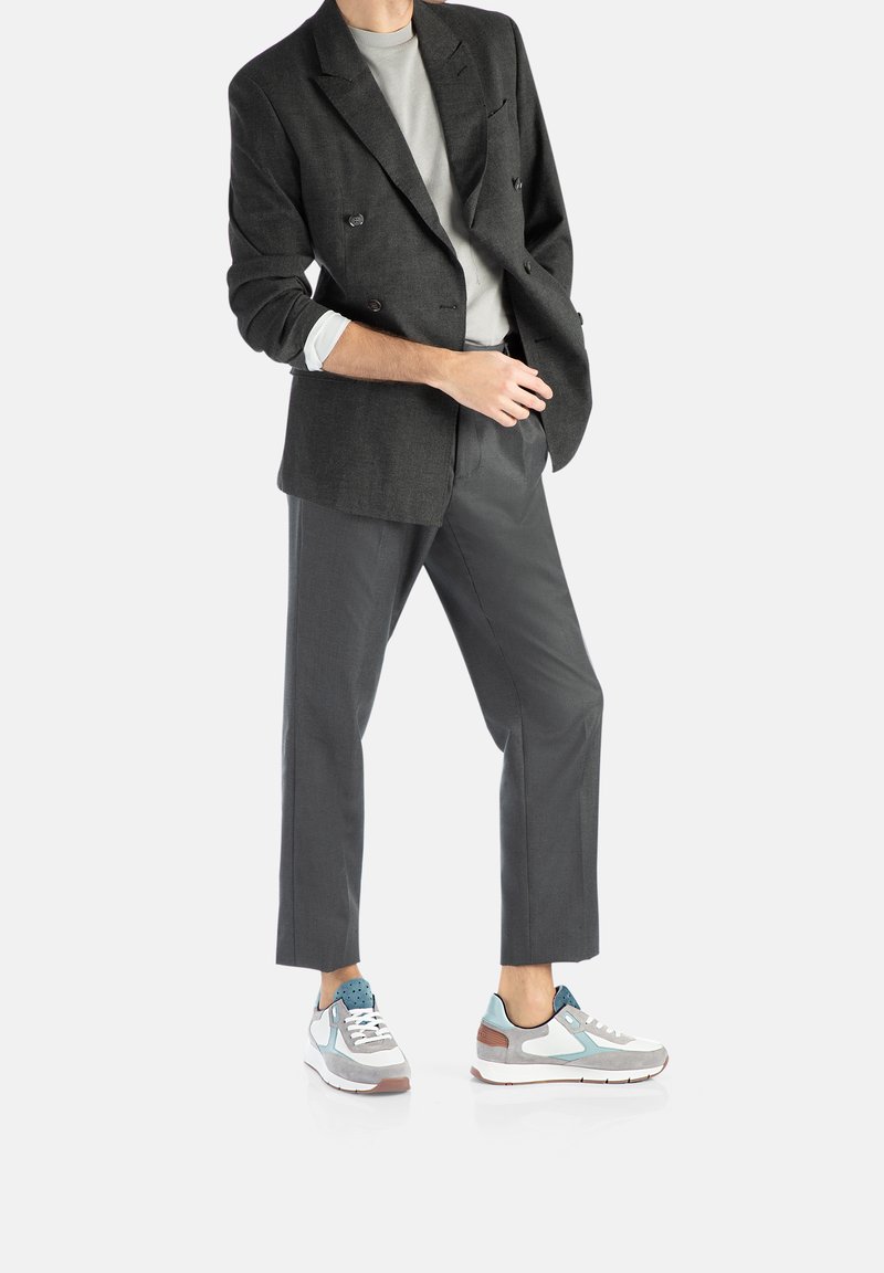 Grau gestreifter Doppelreiher-Blazer über einem hellgrauen Hemd, kombiniert mit maßgeschneiderten grauen Hosen und mehrfarbigen Sneakern mit blauen Akzenten.