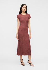 Robe midi côtelée couleur rose foncé, silhouette ajustée avec manches courtes et finition texturée, associée à des escarpins noirs à lanières.