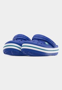 Ζευγάρι μπλε παπούτσια τύπου σλίπ-ον με τρύπες για αερισμό, λευκές και τυρκουάζ ριγωτές σόλες, και ρυθμιζόμενα λουράκια στη φτέρνα πάνω σε λευκό φόντο.