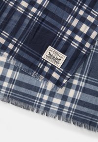 Marineblå og lyseblå rutete skjerf laget av stoff med frynsete kanter. Har et etikett fra Levi Strauss & Co. med grafikk og tekstdetaljer.
