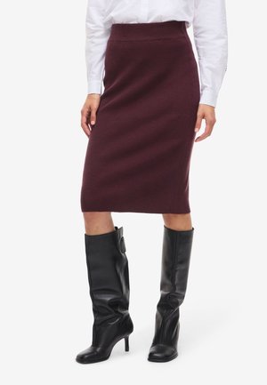 Bordeaux ribbelpencilrok met een aansluitende taille, gecombineerd met glanzende zwarte knielange laarzen met een puntige neus en een hoge hak.