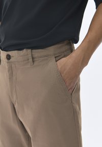 Beige katoenen broek met een reguliere pasvorm, voorzien van zijzakken, een knoopsluiting en zichtbare stikseldetails.
