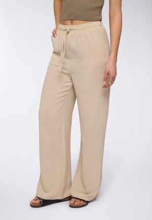 Pantaloni beige a gamba larga realizzati in tessuto leggero, con cintura elastica e cordoncino regolabile, tasche laterali e una texture liscia.
