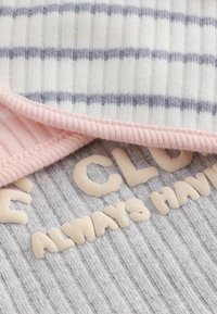 Des morceaux de tissu multicolores : une texture côtelée rayée blanche et bleue, un bord côtelé rose clair et une base grise douce avec des lettres en relief.