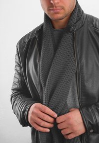 Black leather jacket over a gray textured sweater, featuring a dark gray knit scarf draped around the neck. Hands adjust the scarf.