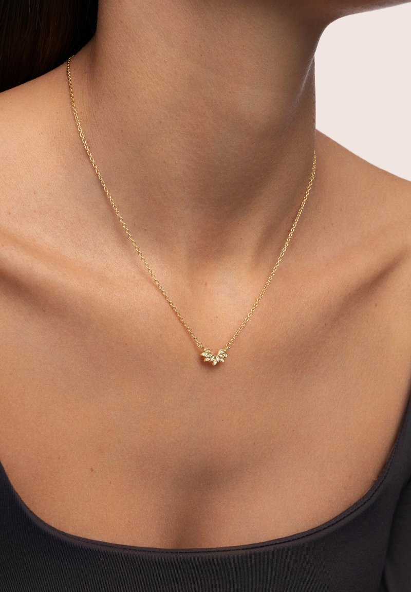 Collier en or avec un pendentif floral orné de petites pierres précieuses transparentes ; chaîne délicate avec des maillons, portée contre la peau.