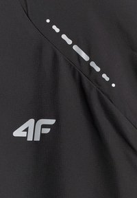 Tissu noir avec logo argenté « "4F" » et rangée diagonale de points ovales réfléchissants pour la visibilité, probablement partie d'une veste de sport.