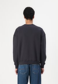 Mørkegrå sweatshirt med avslappet passform, rund hals og senket skuldre. Har ribbestrikkede mansjetter og nederkant. Brukes sammen med blå denimjeans.