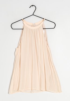 Jasno brzoskwiniowy bezrękawnik z okrągłym dekoltem, marszczonym materiałem i otworami bocznymi. Wykonany z miękkiego, lekkiego materiału. Wisi na czarnym wieszaku.
