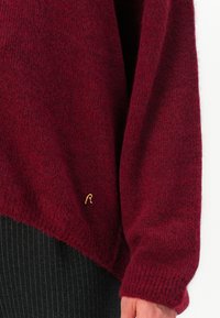 Maglione lavorato a maglia bordeaux con una texture morbida, caratterizzato da un logo "R" ricamato in oro sull'orlo. Design comodo e morbido con maniche ampie.