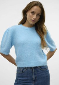 Gaiši zila adīta džemperis ar īsām pūkainām piedurknēm un ribotu apakšmali. Materiāls izskatās mīksts un pūkains, radot siltu tekstūru.