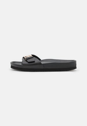 Black open-toe slide sandal with wide strap and gold-tone decorative buckle, flat sole, displayed on white background.