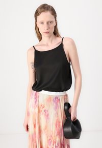 Schwarze Satin-Camisole mit Spaghettriemen, kombiniert mit einem gefalteten pastellfarbenen Blumrock, hält eine schwarze Lederhandtasche.