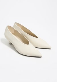 Zapatos de tacón blancos de punta afilada con un bajo tacón de kitten, textura suave y diseño minimalista. Forro interior y forma estructurada para mayor soporte.