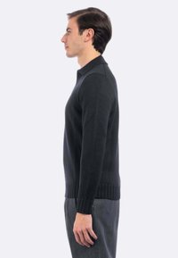 Maglione nero lavorato a maglia con colletto a polo, polsini e orlo a coste. Mostrato su un modello di lato, che indossa pantaloni grigi.