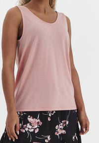 Top rosa senza maniche con scollatura arrotondata, realizzato in un tessuto liscio, abbinato a una gonna nera a fiori con accenti bianchi e rosa.