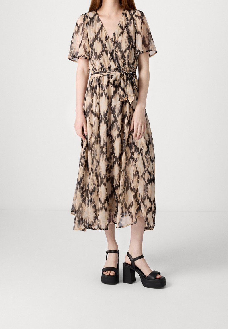 Vestido maxi con diseño envolvente, que presenta un estampado animal en beige y negro, mangas cortas y un cinturón de lazo. Combinado con sandalias de plataforma negras.