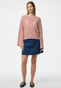 Top a righe rosso e bianco con maniche lunghe, abbinato a una gonna in denim blu, caratterizzato da una vestibilità rilassata e maniche a campana, con scarpe flat nere.