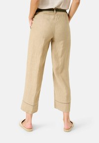 Beige linne beskjärda byxor med en avslappnad passform, med en vikbar fåll och subtila sömnadsdetaljer. Matchas med platta, öppna skor.