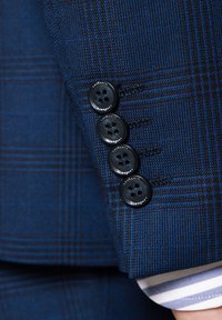 Granatowa, dopasowana marynarka w kratę, z czterema czarnymi guzikami na mankietach oraz kontrastową, paskowaną podszewką w rękawie.