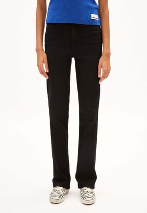 Black straight-leg jeans made of cotton denim, with a high waist, classic front pockets, and subtle stitching details. Paired with striped sneakers.