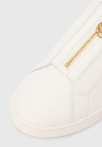 Baskets blanches avec une finition en cuir lisse, dotées d'une fermeture éclair dorée sur le côté et de coutures contrastées. Conception à bout arrondi.