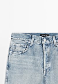 Light blue denim jeans with a mid-rise waist, five-pocket design, and metal hardware. Label reads "Massimo Dutti." Smooth texture and straight cut.